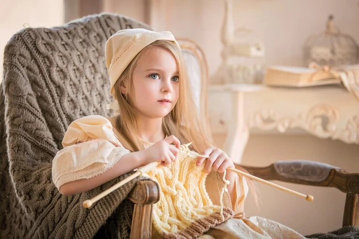 liten jente i lyse vintageklær som strikker